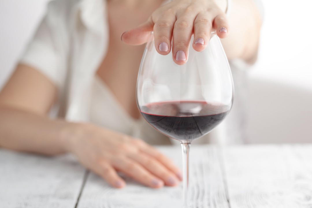 Hand covering a glass of red wine
